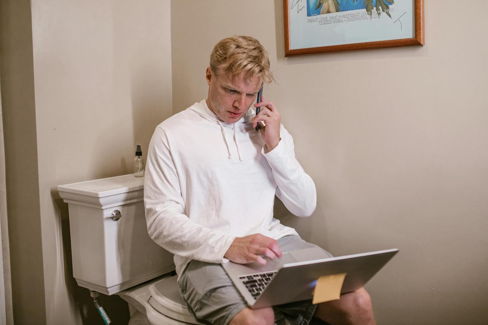 Man Sitting on Toilet Using Laptop and Phone